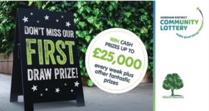 A black sandwich board sign reading "Don't miss our first draw prize!" in green and white lettering, next to a white bubble reading "Win cash prizes up to £25,000 every week plus other fantastic prizes" in black and green lettering.