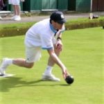 A lawn bowler dressed in white about to take his shot